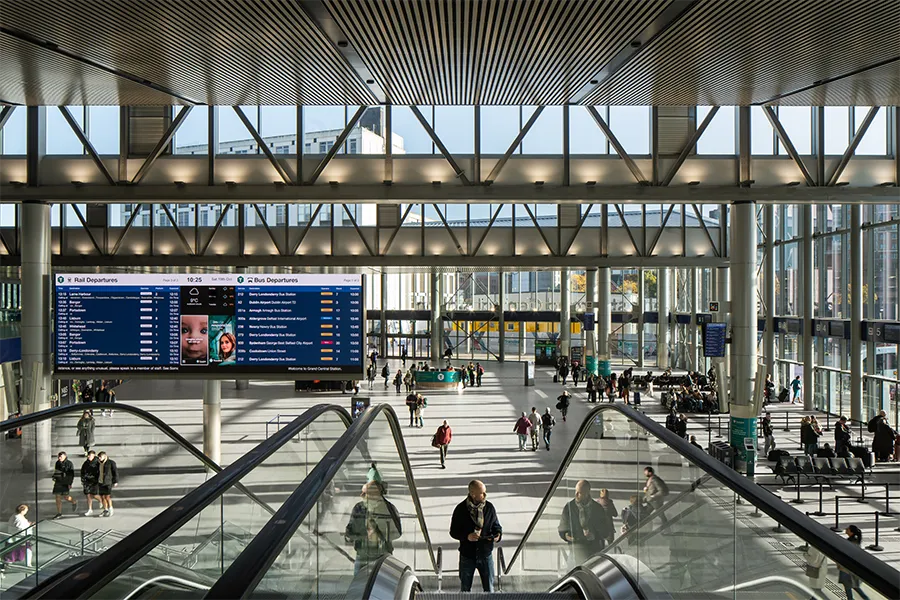 People walking through the bright concourse of Belfast Grand Central Station surrounded by modern architecture.