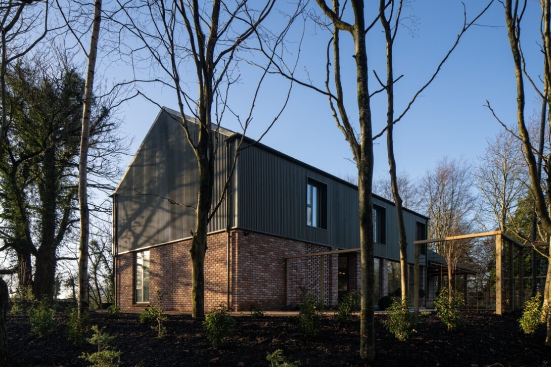 Exterior of The Chalet by Nest Architects in early morning light, showing corrugated green façade and brick detailing — UK architectural photography.